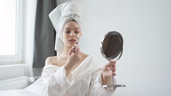 Goodlooking Happy Woman with Towel on Head Holding Mirror and Applying Make Up with Brush