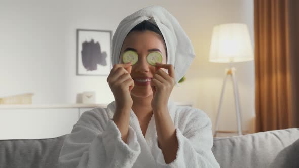 Zoom in Portrait of Pretty Asian Woman in Bathrobe with Towel on Head Putting Fresh Cucumber Slices alt