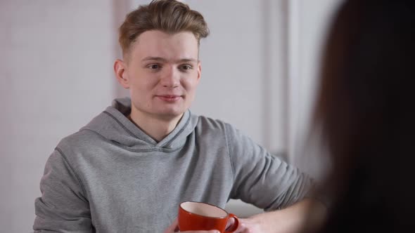 Portrait of Young Happy Loving Man Talking with Woman and Drinking Coffee in Cafeteria alt
