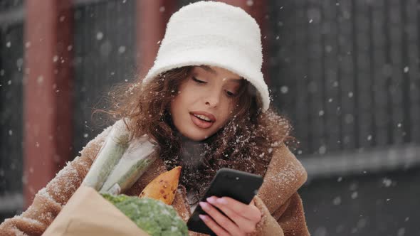 A Woman is Standing Near a Supermarket and Texting on a Smartphone alt