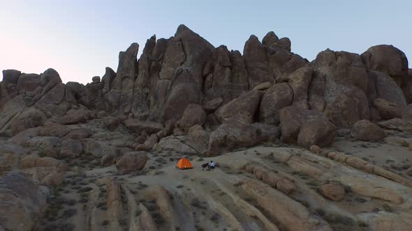 Aerial shot of a young man backpacker camping with his dog in a mountainous desert. alt