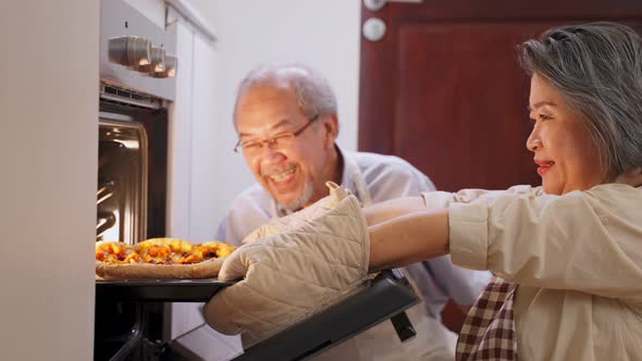 Asian senior older grandparents making pizza, bring the food out from oven machine together at home. alt