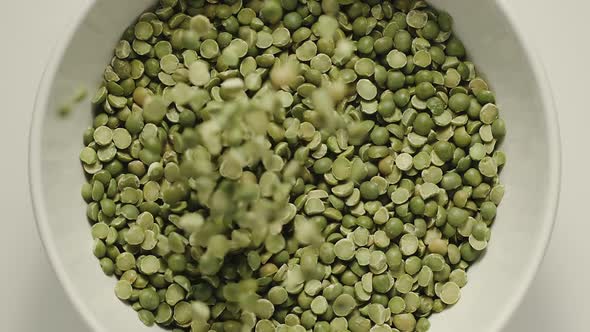 Green peas falling into a white bowl