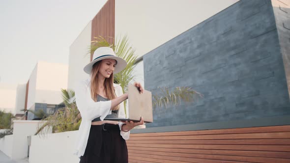 Attractive Woman Standing Outdoors with Laptop in Hands alt