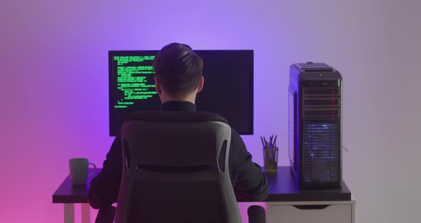 Rear View of Man Programmer Coding Network Security Software Indoors in Neon Lights at Night alt