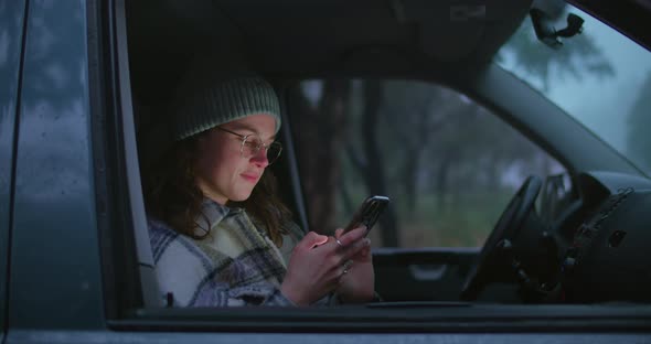 Woman Sit Inside Car Screen Lit Face with Phone alt