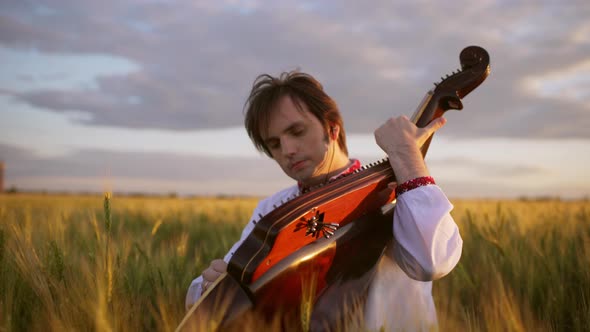 Slow Motion of Young Man Bandurist in Ukrainian Vyshyvanka Surrounded with Wheat on Grainfield