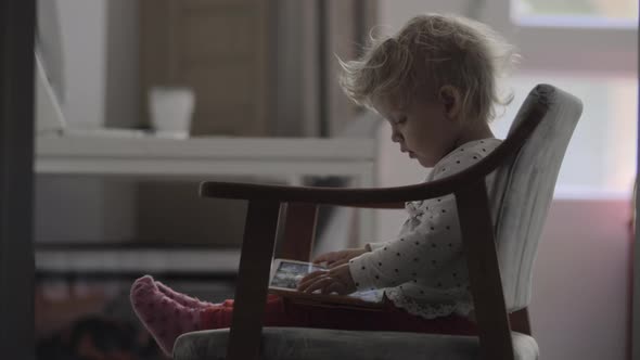 A baby girl sitting in a chair with a tablet on her laps alt