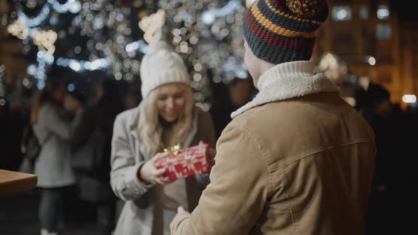 Man Standing Back to Camera Presents a Gift to Her Girlfriend at Xmas Night at Old Town Square alt