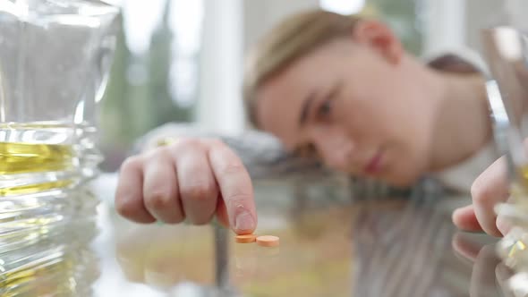 Male Finger Moving Pill on Glass Table with Blurred Sad Face of Young Addicted Man Lying at alt