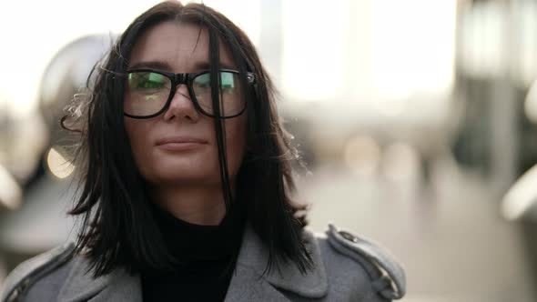 Portrait of a Brunette with Glasses on a Background of Blurred Metal Structures alt