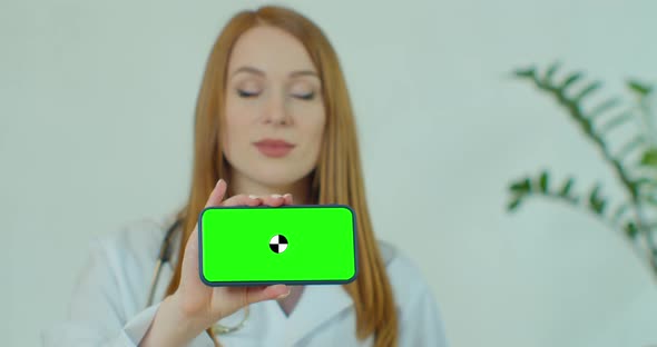 Female Medical Professional Displaying Mobile Smartphone with Greenscreen. Woman Doctor Holding