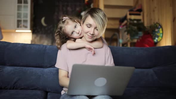 Mom Is Trying To Work on Laptop with Her Daughter Cuddling Her in Living Room