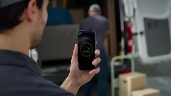 Rear view of delivery man holding mobile with mobile app. Shot with RED helium camera in 8K. alt