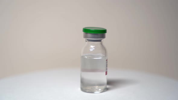 The glass bottle with the liquid rotates on a turntable. The vaccine against COVID-19.