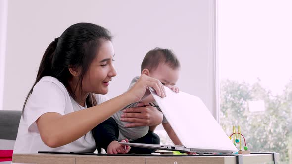 Happy Young Mother with a Child Working at a Computer, Single mom freelancer concept.