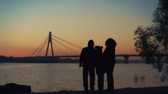 Parents Kid Silhouette Watching Sunset Standing Together at River Bridge View alt