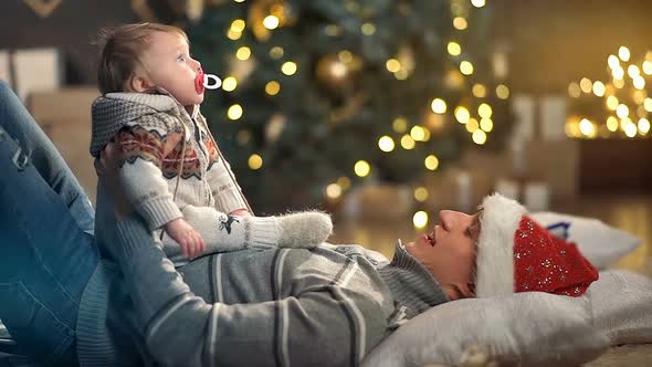 Happy Father and Adorable Newborn Baby Playing in Front of Christmas Tree alt