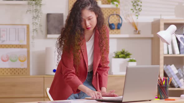 Young entrepreneur working standing at desk at home office arranging papers alt
