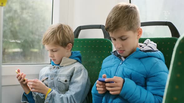 Two Boys In The Passenger Seat On The Bus Playing Smartphones. alt