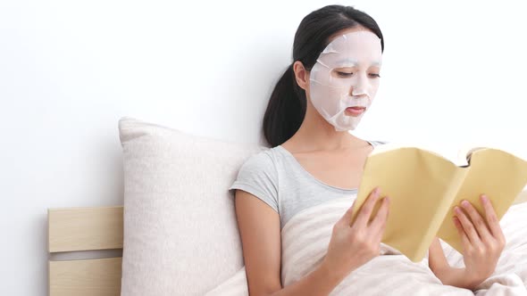 Woman use of paper mask on face and read book on bed  alt