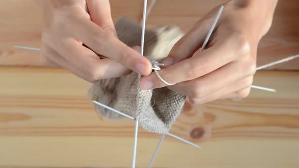 young womans hands knitting with gray metal needles and woolen thread on wooden table background