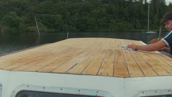 Wiping down sanded roof of wooden boat with cloth and paint thinners alt