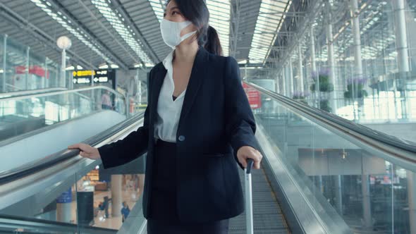 Asian business girl wear face mask drag luggage stand on escalator look around walk to terminal.