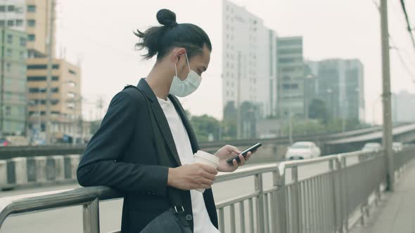 Asian businessman wearing a face mask holding coffee cup and using phone.