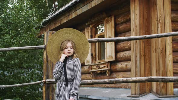 Young Country Girl in Hat Posing on Wooden Rustic House Background. Beautiful Teenager Girl in Hat alt