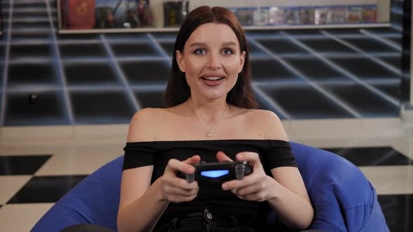 A Young Woman Plays Video Games While Sitting in an Easy Chair in the Game Room alt