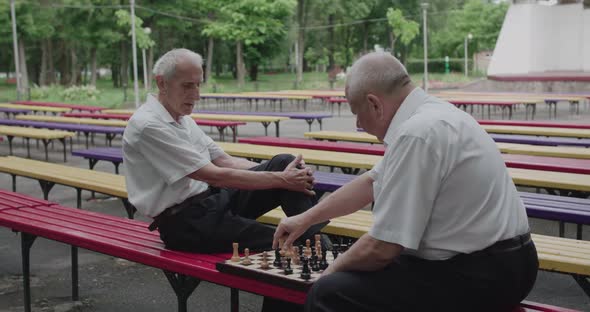 View of Chess Game Between Elder Thoughtful Men Having Relax on Outdoors Bench alt