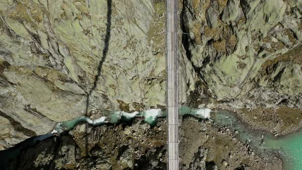 Aerial top down shot of high bridge between mountains and river on ground alt
