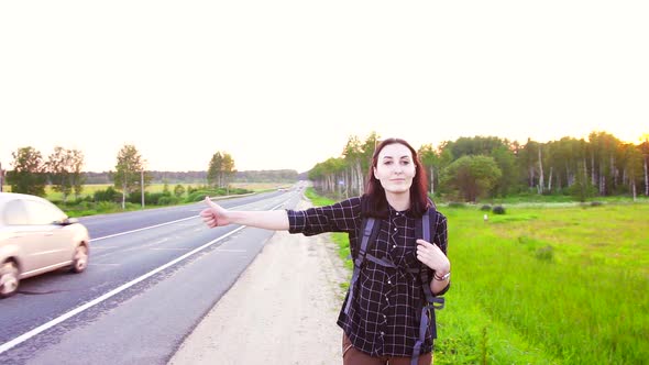 Portrait of a Girl Tourist with a Backpack on the Highway Hitching a Ridethumb Up alt