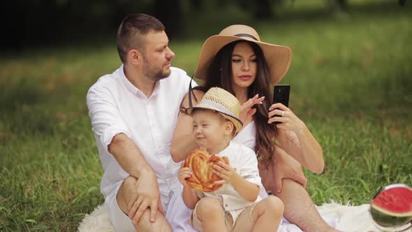 Beautiful Husband and Cute Wife Take Selfies in the Park Whith Their Little Child