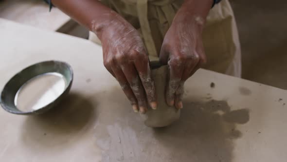 Close up view of female potter wearing apron working on clay to create pot at pottery studio alt
