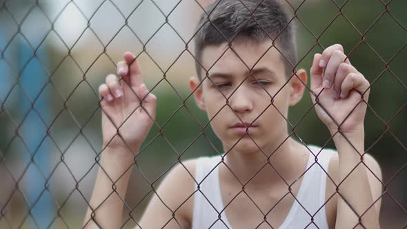 Refugee Serious Boy Stands Alone Head Bowed Near the Fence Regrets Actions
