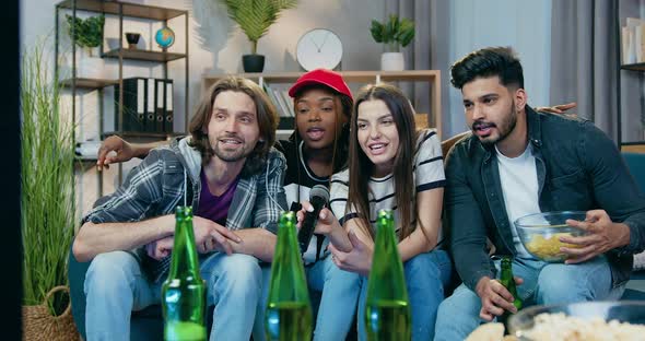 Friends Sitting in front of Karaoke Setup and Singing Songs in Microphone During Cheerful Home Party alt