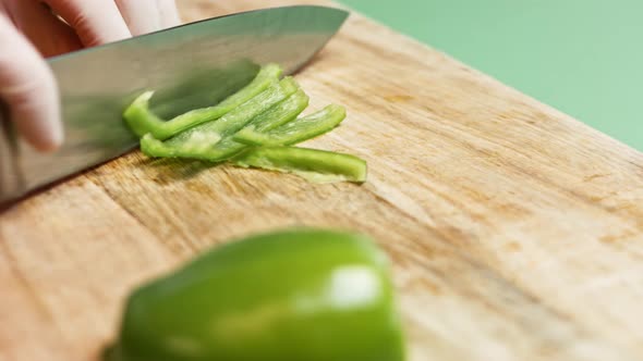 Top view on dark-skinned man hands by knife cut on slices big green bell pepper alt