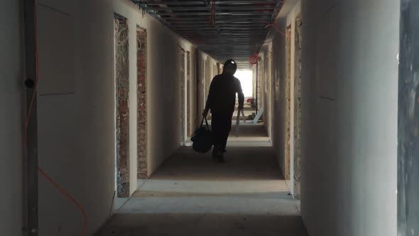 Silhouette of a Construction Worker Walking Down a Dark Corridor with a Tool in His Hands alt