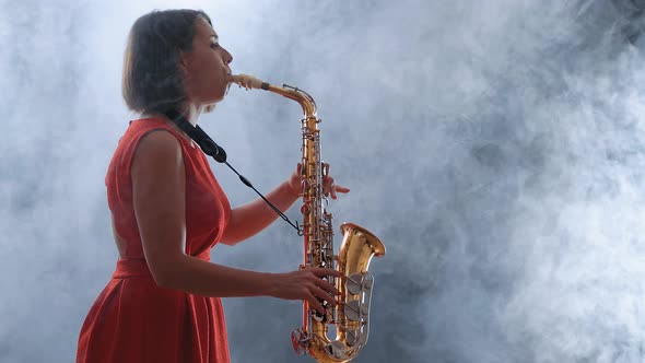 Beautiful Woman in Red Dress Playing a Melody on Saxophone. Smoky Dark Studio