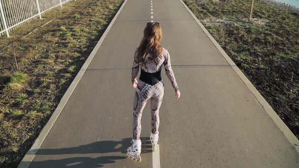 Athletic slender girl rollerblading on the path along the lake. Slow motion. Top view alt