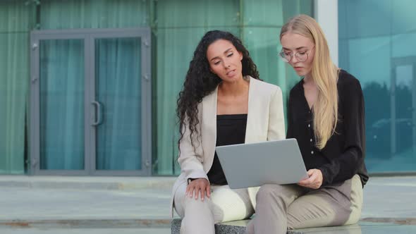 Two Diverse Businesspeople Chatting Sitting Behind Laptop Outdoors alt