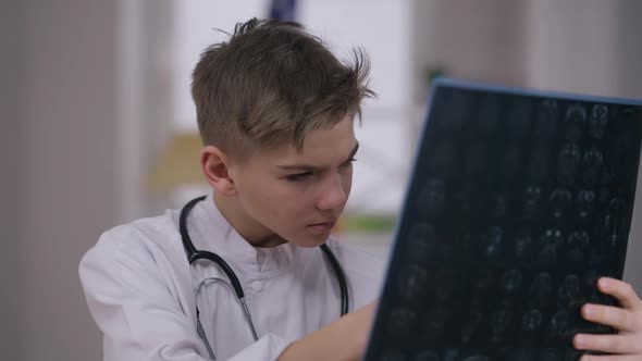 Thoughtful Little Doctor in White Medical Gown Examining Xray with Magnifying Glass alt