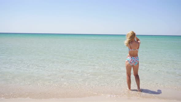 Rear View of an Unrecognizable Woman in a Bathing Suit Standing in the Azure Sea Looking Around