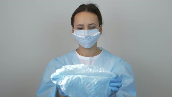 Female doctor puts on medical cap before surgical treatment in clinic wearing mask and latex gloves alt