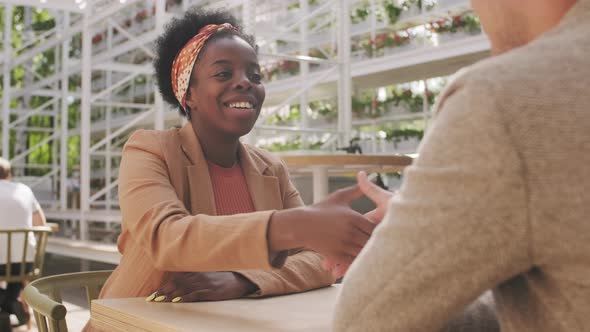  Black Businesswoman Shaking Hands with Businessman in Cafe alt