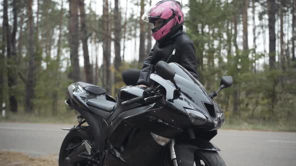 Confident Young Woman Approaching Motorbike, Sitting on It, and Closing Helmet Visor. Portrait of alt