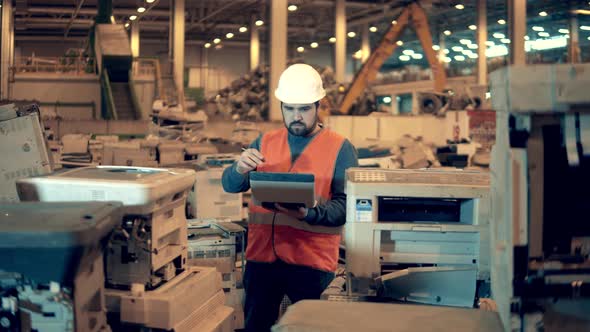 Junkyard Worker is Inspecting Thrownout Office Machines alt