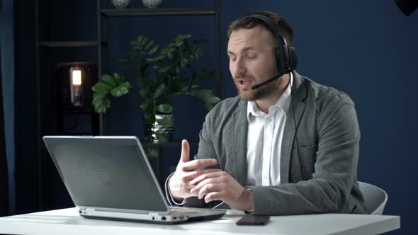 Young Business Man in a Headset Sitting at an Office Table in Front of a Laptop